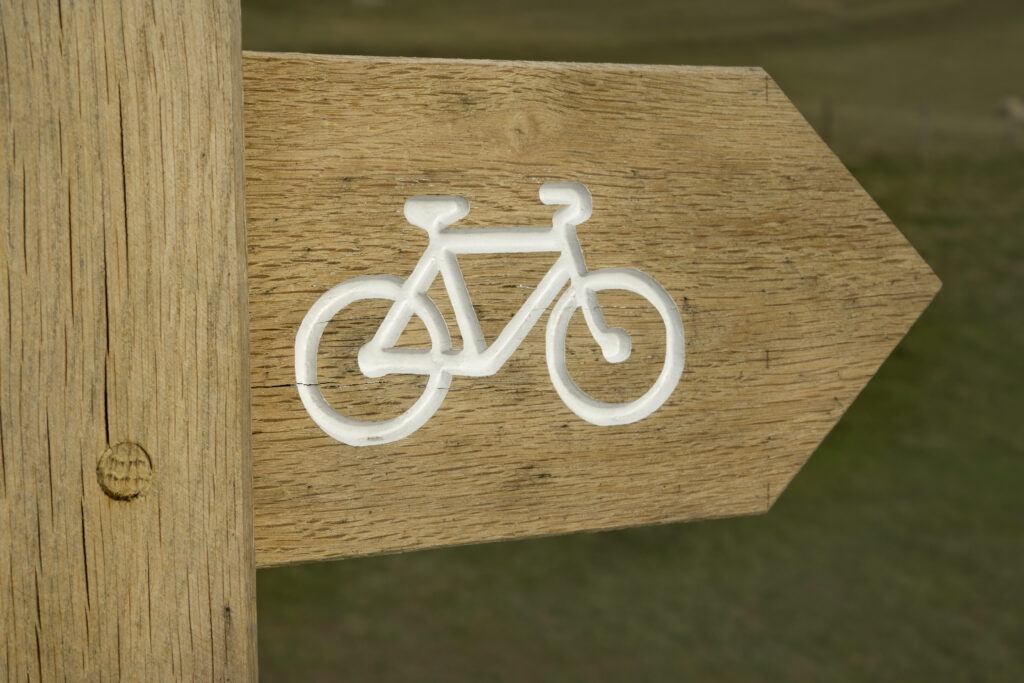 wooden sign with bicycle symbol, pointing to cycle path